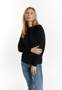 Felpa nera con maniche lunghe e scollatura rotonda. Realizzata in tessuto morbido, presenta una vestibilità rilassata e polsini e fondo a costine.
