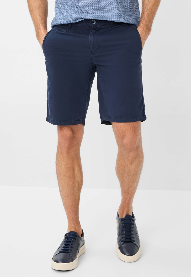 Pantaloni corti blu navy realizzati in tessuto liscio, con un taglio dritto, tasche laterali e una cintura discreta. Abbinati a sneakers blu scuro.