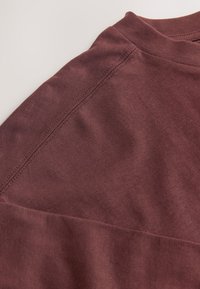 Gros plan d'une chemise en tissu bordeaux montrant des coutures détaillées le long de la couture de l'épaule et de l'encolure.