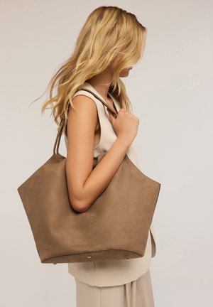 Große taupefarbene Tote-Tasche aus weichem Wildleder mit minimalistischer Gestaltung, ausgestattet mit Doppelgriffen und Akzenten aus goldfarbenem Metall.