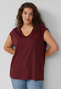 Bordeaux kortemouwen top met een V-hals ontwerp, gemaakt van zachte stof, met een relaxte pasvorm en een gladde textuur, gecombineerd met lichtblauwe jeans.