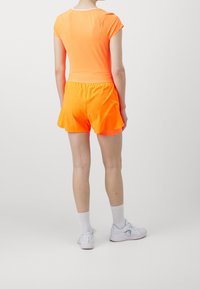 Oranssi urheilupaita ja shortsit, joissa on tiivis muotoilu. Materiaali näyttää sileältä ja joustavalta. Yhdistetty valkoisten sukkien ja vaaleiden lenkkarien kanssa.