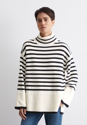 Sweter z kołnierzem typu golf w kremowo-czarny paski, o luźnym kroju, szerokich rękawach i prążkowanej fakturze. Noszony z dżinsami.