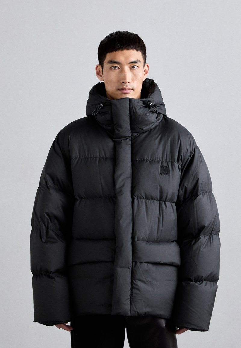 Chaqueta acolchada negra con un alto cuello, diseño de acolchado horizontal y dos bolsillos frontales. Presenta detalles con cordones y un ajuste relajado.