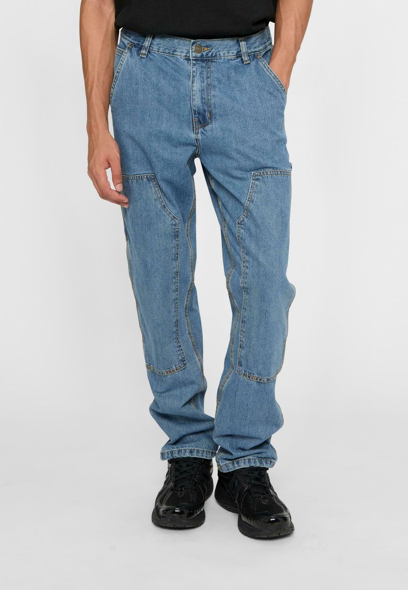 Light blue denim pants with a loose fit, featuring multiple front pockets, reinforced stitching, and a button closure at the waist.
