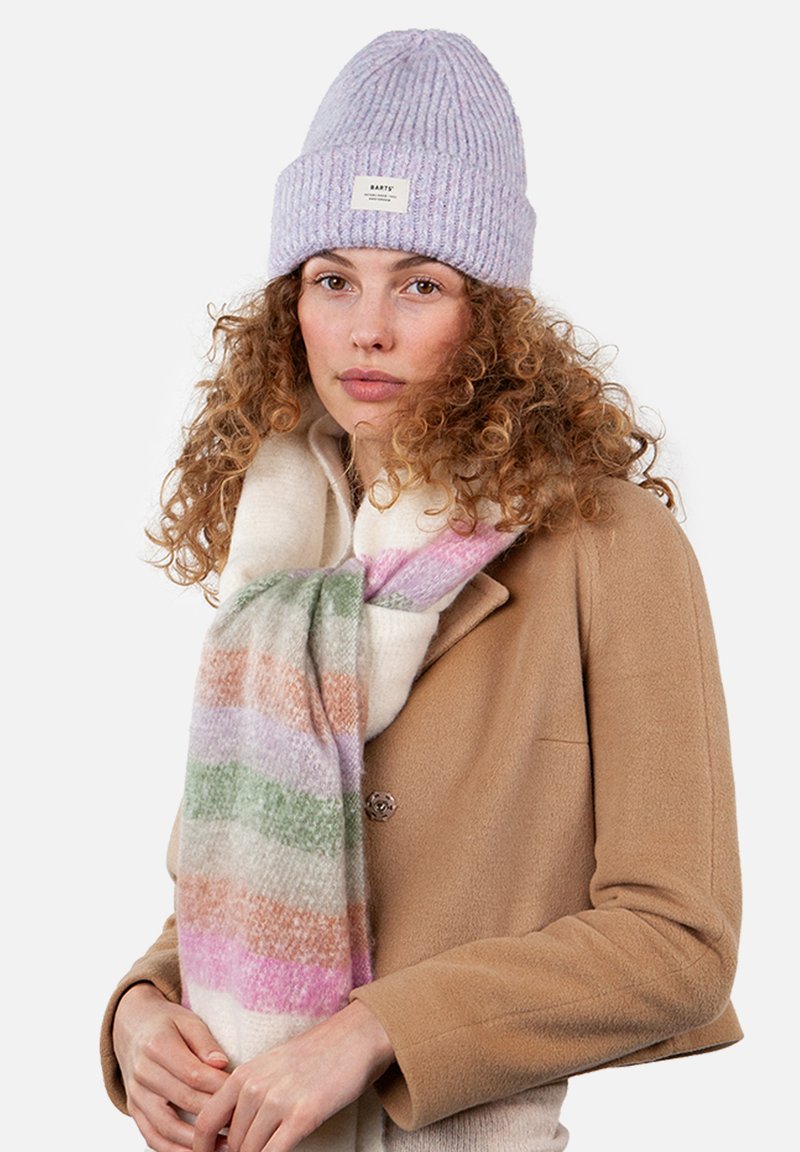 Lavendel ribbenstrikket hue og et multicolor stribet halstørklæde i pink, grønne og orange nuancer, båret over en brun frakke.
