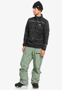 Fleecepolo med svarta tribal mönster, dragkedja i nacken, kombinerad med ljusgröna cargobyxor med flera fickor och svarta snowboard boots.