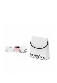 Bolsa de regalo de papel blanco con asas de cuerda negra, con el logo de "PANDORA". Dos pequeñas cajas de joyería blancas, una con un interior rosa, ligeramente abiertas.