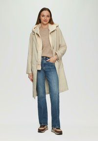 Beige Karo-Mantel mit einer weichen, cremefarbenen gefütterten Kapuze, langen Ärmeln, Seitentaschen, kombiniert mit blauen Jeans und braunen Sneakers.