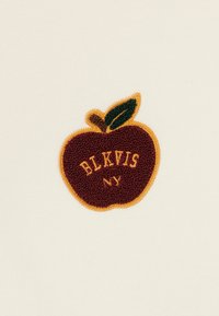 Εμπριμέ λάδι μήλου σε κρέμα ύφασμα; Το μήλο είναι σκούρο κόκκινο με ένα πράσινο φύλλο, περιγραμμένο σε κίτρινο, με το κείμενο "BLKVIS NY."