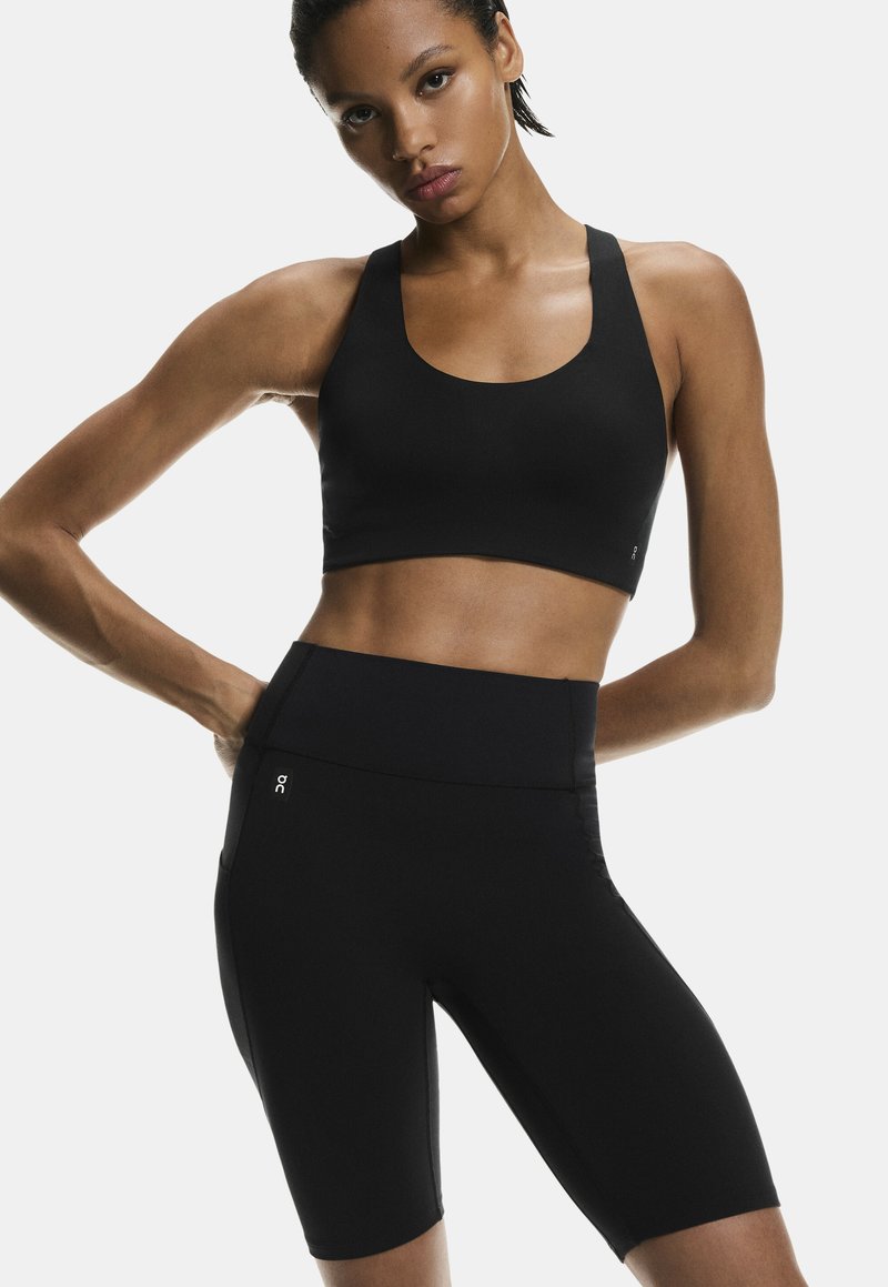 Sujetador deportivo negro y pantalones cortos de talle alto en una tela suave y elástica. Presenta un escote redondo y detalles con logo en la cinturilla.