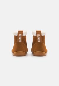 Bottes de cheville en suede beige avec doublure en fausse fourrure blanche, présentant une boucle arrière proéminente étiquetée "CAMPA", et une semelle flexible et arrondie.