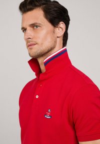 Polo rosso con colletto strutturato, dettagli a strisce bianche e blu, tre bottoni e logo ricamato sul petto.