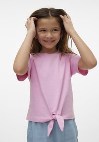 T-shirt en coton rose clair avec des manches courtes, présentant un ourlet noué à l'avant. Le t-shirt a un col rond et une coupe décontractée.