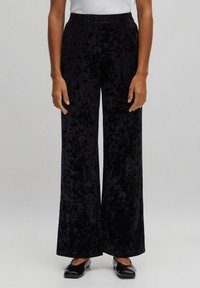Pantalons large en velours noir avec une texture lisse et une taille haute. Design long au sol, style minimaliste, sans motifs ni accents visibles.