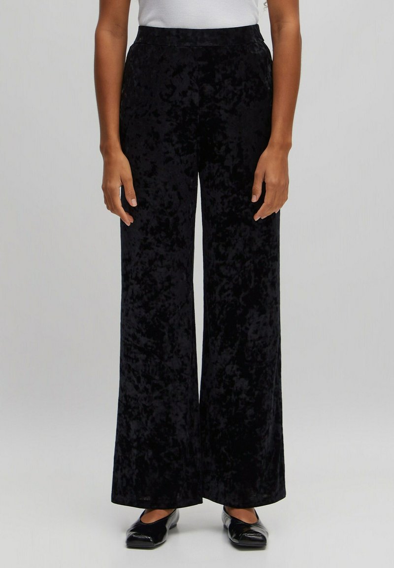Pantalons large en velours noir avec une texture lisse et une taille haute. Design long au sol, style minimaliste, sans motifs ni accents visibles.