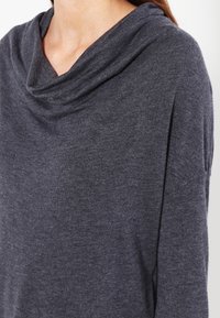 Mörkgrå kofta med cowl-halsringning gjord av mjukt stickat tyg, med lös passform och draperad design, synlig textur och subtil lyster.