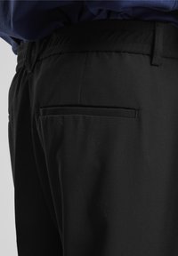 Gros plan d'un pantalon noir avec une ceinture et une poche arrière fendue, porté avec un haut bleu foncé.