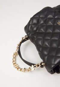 Bolso de mano de cuero negro acolchado con cadena dorada y asa de cuero negro, que presenta una textura suave y un destacado detalle de costura.