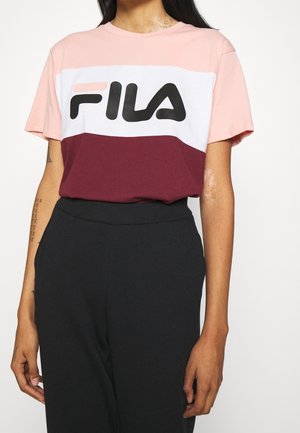 Personne portant un t-shirt FILA color-block rose, blanc et bordeaux avec un pantalon noir taille haute sur fond blanc.