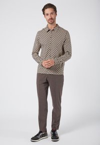 Langemouwen shirt met een geometrisch patroon in geel, blauw en zwart; gecombineerd met bruine broeken en zwarte sneakers. Eenvoudig kraagontwerp.