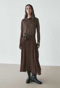 Brown long-sleeve top with loose fit, paired with a textured brown skirt featuring a dotted pattern, and black knee-high boots.