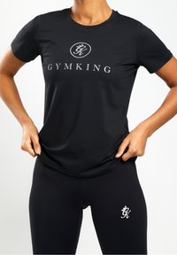 Černé sportovní tričko s krátkým rukávem, se stříbrným logem "GYMKING" a hladkým, elastickým materiálem. V kombinaci s černými legínami.