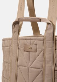 Bolso tote acolchado beige con un patrón de diamantes, que cuenta con resistentes asas de tela y una etiqueta de cuero con el logo "BOSS" en relieve.