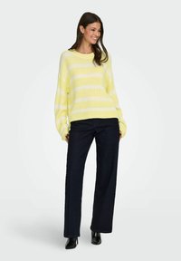 Gelb-weiß gestreifter, gestrickter Pullover mit lockerem Schnitt und gerippten Bündchen, kombiniert mit dunkelblauen, weiten Jeans und schwarzen, hohen Stiefeln.