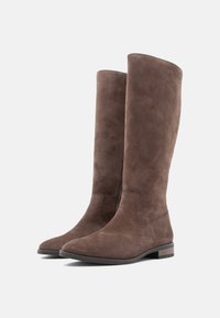 Barna velúr, térd fölé érő csizmák alacsony, tömör sarkú és kerek orrú kialakítással, egymás mellett elhelyezve semleges háttér előtt.