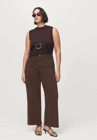 Top sin mangas marrón combinado con pantalones amplios marrones, con un dobladillo sin rematar, y sandalias negras de tiras. Acabado con un collar de colgante circular negro.