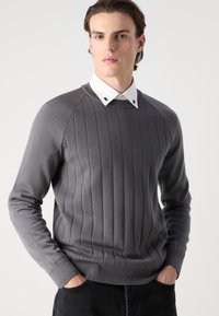 Grauer gerippter Strickpullover mit rundem Ausschnitt, langen Ärmeln und einem kontrastierenden weißen Hemd darunter.