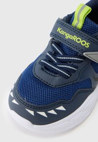 Μπλε αθλητικά παπούτσια από δίχτυ και συνθετικά υλικά με γκρι λεπτομέρειες, λευκή σόλα, ελαστικά κορδόνια και αναγνωρίσιμο σχέδιο με δόντι καρχαρία στη μύτη. Επωνυμία KangaROOS.