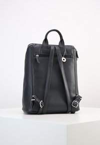 Sac à dos en cuir noir avec des bretelles doubles, une poignée supérieure, une fermeture éclair et une poche arrière avec un petit accent porte-clés.