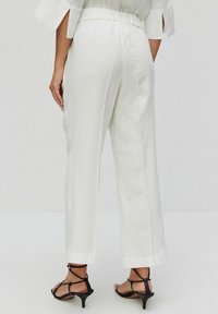 Witte linnen wijde pijpen met een elastische tailleband en zijzakken, gecombineerd met zwarte sandalen met hakken en bandjes.
