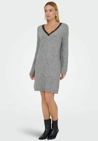 Vestido de punto gris con mangas largas, escote en V adornado con detalles de encaje negro y un corte relajado, combinado con botas negras de tobillo.