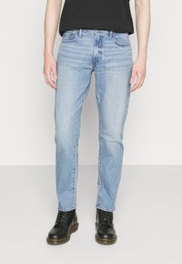 Jeans de mezclilla azul claro con un corte recto, textura desgastada, sutiles arrugas y diseño de cinco bolsillos. Combinados con botas negras de cordones.
