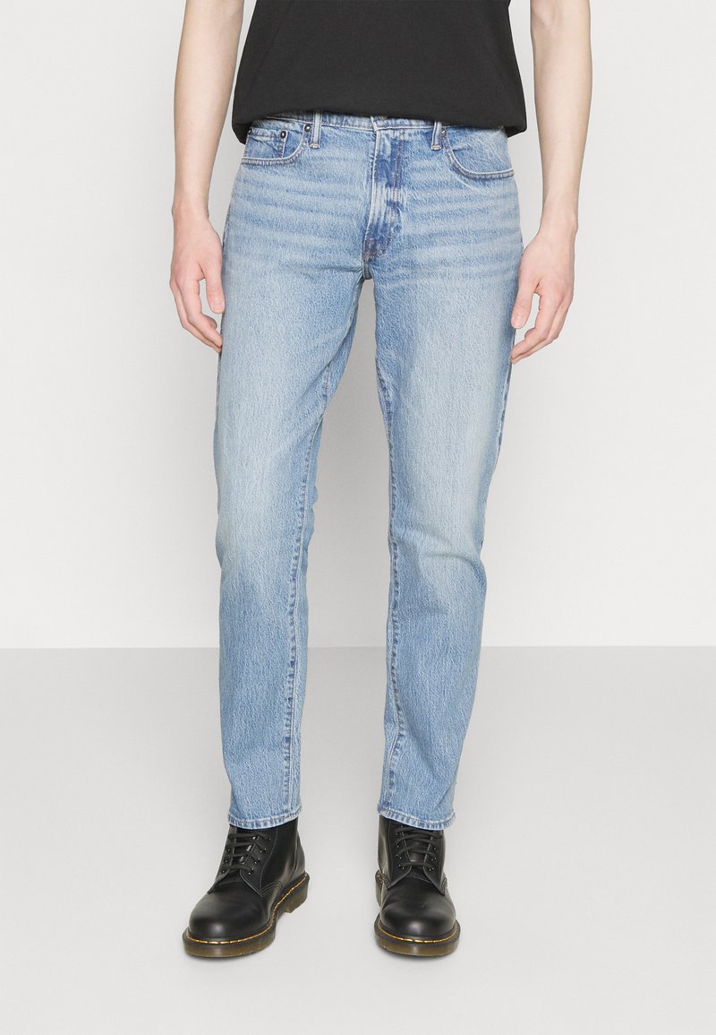 Jeans de mezclilla azul claro con un corte recto, textura desgastada, sutiles arrugas y diseño de cinco bolsillos. Combinados con botas negras de cordones.
