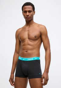 Boxers noirs Nike avec une ceinture turquoise portant le logo Nike. Tissu doux avec un ajustement confortable, ouverture à l'avant et sans motifs.