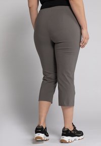Pantalons gris jusqu'aux chevilles en tissu lisse et à la coupe ajustée, associés à des baskets noires pour le sport avec des semelles blanches et beige.
