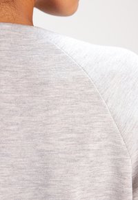 Gray knit fabric showing a close-up of a shirt's back neckline, featuring a subtle texture and seamless shoulder design.