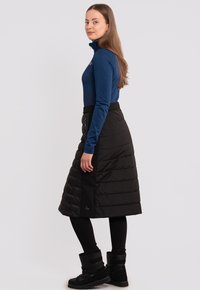 Top azul de manga larga con cuello alto y textura estampada; falda negra abullonada hasta la rodilla con cremallera lateral; combinada con botas negras.
