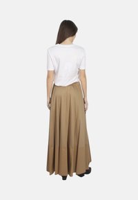 Długa, zwiewna beżowa spódnica z marszczoną talią, zestawiona z prostą białą koszulką. Gładki materiał i plisowany krój podkreślają elegancję.