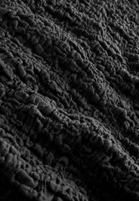 Tissu noir texturé avec une apparence fripée, présentant des motifs en relief et une surface douce et irrégulière, créant profondeur et dimension.
