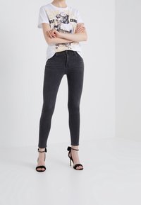 Vit grafisk t-shirt med tryck i svart och vitt, matchad med högmidjade, slim fit, mörkgrå jeans och svarta remsandaler med hög klack.