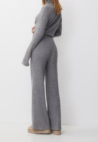 Grijze geribbelde gebreide trui en bijpassende flared broeken, met lange mouwen en een hoge hals. Het materiaal lijkt zacht met een gestructureerde afwerking.