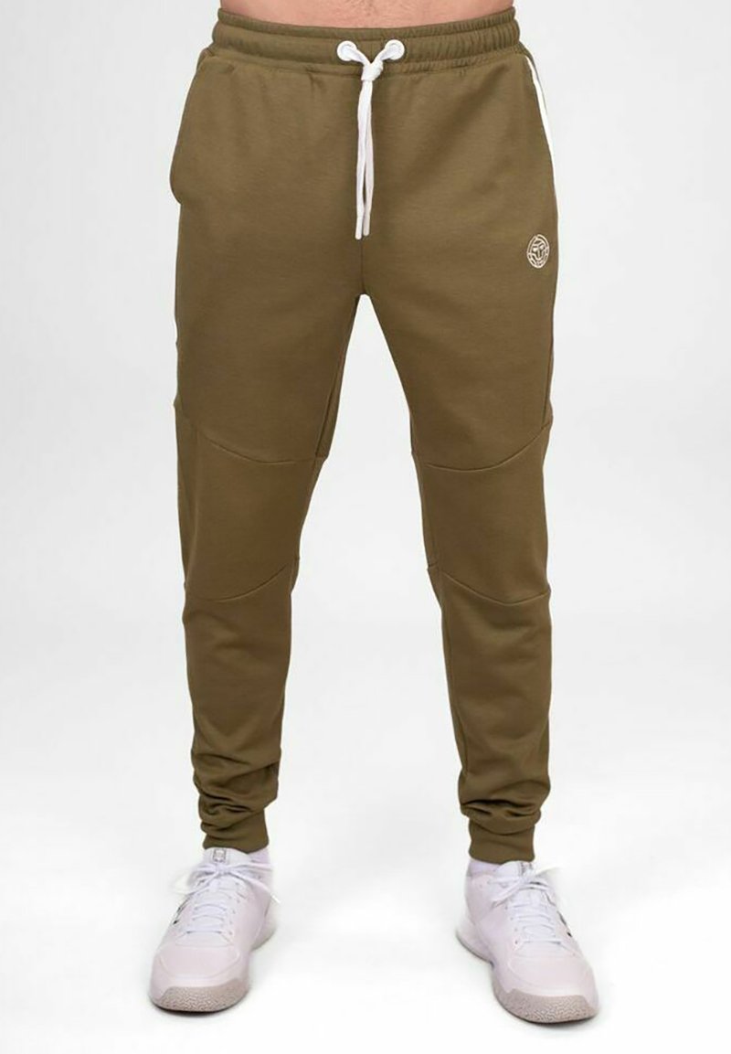 Olivgrüne Jogginghose aus Baumwollmischung mit Bindegürtel, Seitentaschen und Kniefeld-Details. Getragen mit weißen Sneakers.