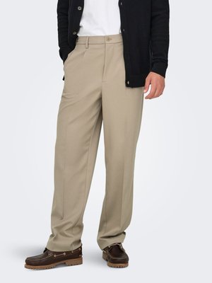 Beige tailored pants with front pleats, a flat front, and side pockets. Paired with a white shirt and a black cardigan. Brown leather shoes.
