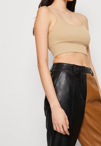 Beige ribbat crop top med tunna remmar, i kombination med högmidjade läderbyxor som har svarta och bruna paneler samt en framficka.