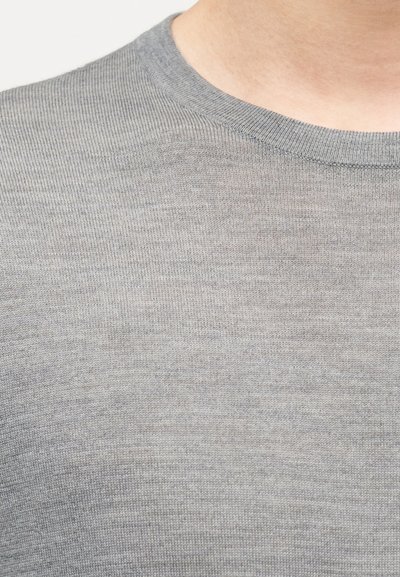 Detailní záběr osoby nosící jednoduchý šedý pletený svetr s kulatým výstřihem, zobrazující krk a horní část hrudi.